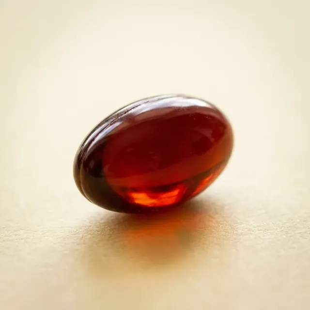 One deep red astaxanthin softgel glowing in warm light